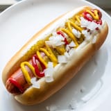 Sizzling Hot Dogs with mustard and ketchup sit in toasted buns, topped with chopped onions and bright green relish.
