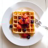 Buttery, golden-brown Waffles topped with fresh strawberries and bananas, served warm on a rustic wooden breakfast table.