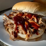Slow-cooked pulled pork sandwich with smoky barbecue sauce, shredded meat, and crisp slaw on a toasted bun.