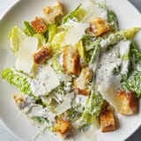 Golden croutons and shaved Parmesan garnish a vibrant bowl of homemade Caesar Salad, ready to serve at a family dinner.