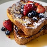 A fork holds a bite of fluffy French toast topped with fresh berries.