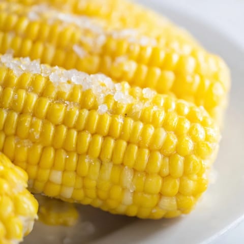 Freshly boiled corn on the cob with melting butter and a sprinkle of sea salt on a rustic plate.