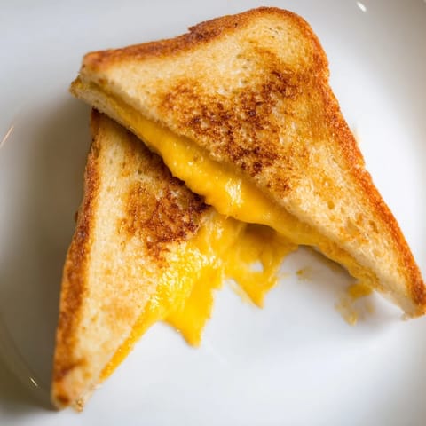 Golden-brown grilled cheese sandwich with gooey melted cheddar on buttery sourdough, cut diagonally and served beside a steaming bowl of tomato soup.