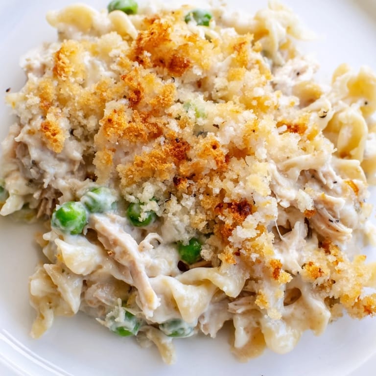 Fork-ready slice of Tuna Casserole lifted from the pan, revealing flaky tuna, sweet peas, and cheesy pasta inside.