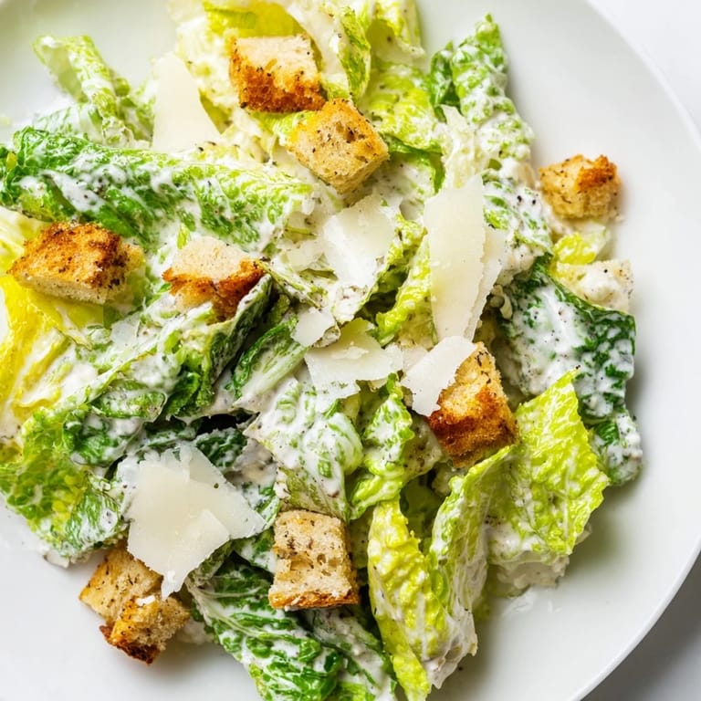 Classic Caesar Salad with bright green romaine leaves, creamy dressing, and crunchy croutons arranged beautifully on a white plate.