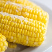 Freshly boiled corn on the cob with melting butter and a sprinkle of sea salt on a rustic plate.