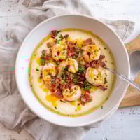 Creamy cheddar grits topped with sautéed shrimp, bacon, and peppers in a savory sauce, garnished with fresh parsley.